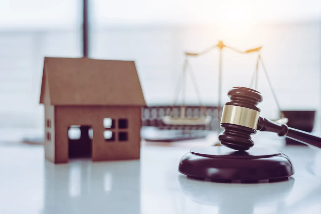 A gavel with a miniture house in the background with scales.