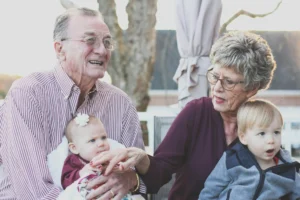 Two grandparents with two grandchildren on the porch of a residential house.