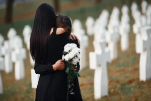 Two people hugging graveside, wearing black.
